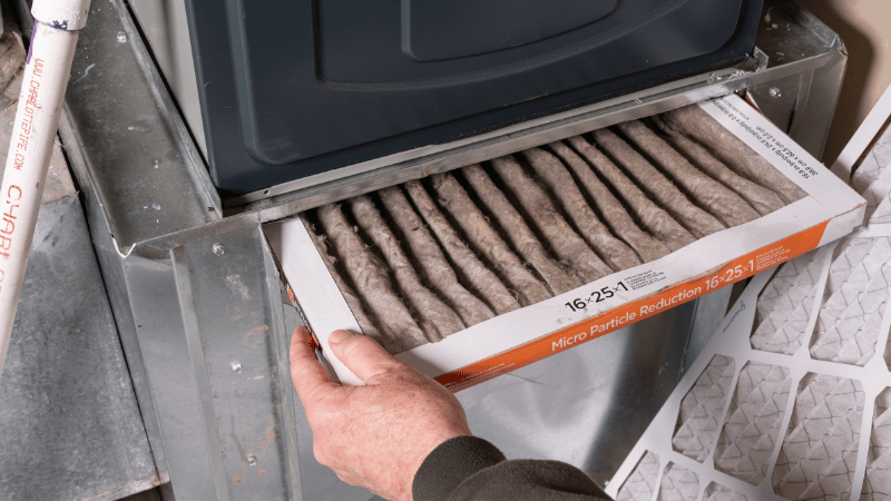 Dirty furnace air filter being removed from an HVAC system, showing heavy dust buildup that restricts airflow and reduces efficiency.