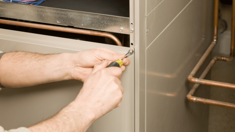 HVAC technician installing a residential furnace by securing the access panel and connecting internal heating components.