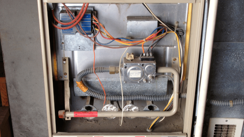 Open residential furnace unit with visible wiring, gas valve, and internal components during inspection or maintenance.