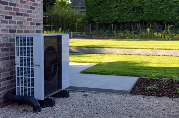 An outdoor air conditioning condenser unit is installed beside a brick home near a landscaped yard.