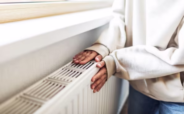 A person warms their hands over a home radiator to stay comfortable during cold weather.