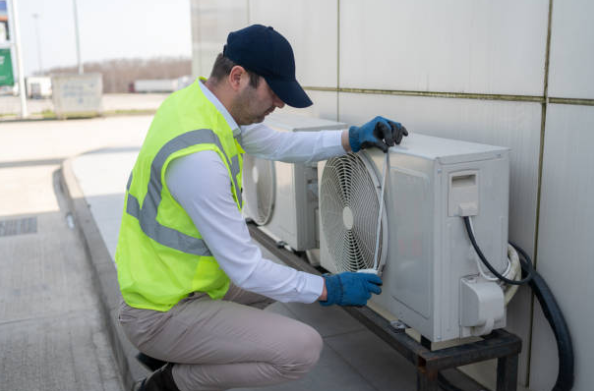 An HVAC technician wearing safety gear services an outdoor air conditioning unit during routine maintenance.