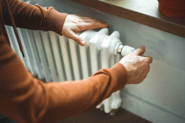 A homeowner adjusts the valve on a white radiator to control the heating inside the room.