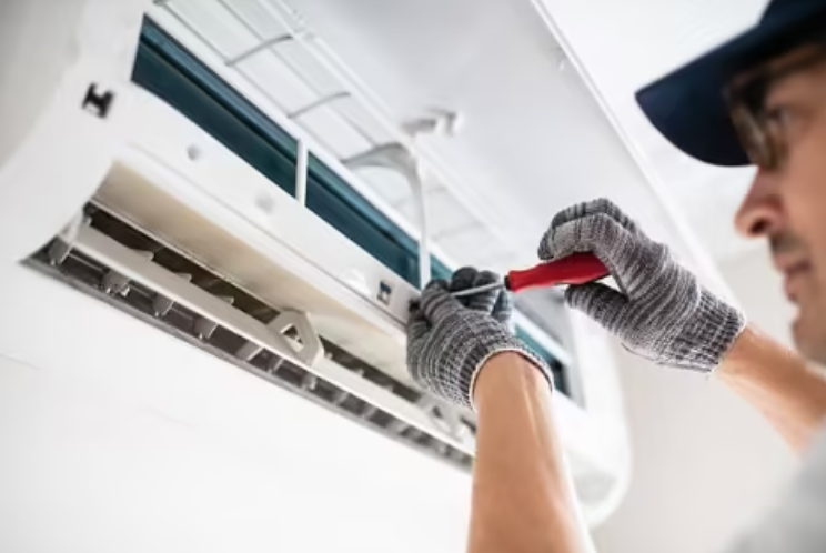 A technician uses a screwdriver to service an indoor air conditioning unit.