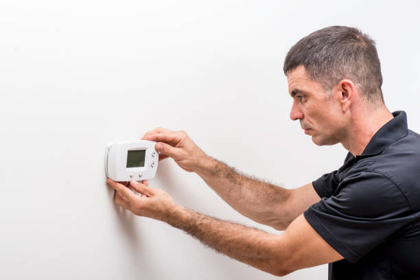 Technician adjusting the settings on a digital wall-mounted thermostat.